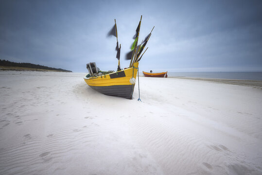 View of a traditional yellow fishing boat resting on the white sandy beach under a dramatic cloudy sky Debki, Pomeranian Voivodeship, Poland.