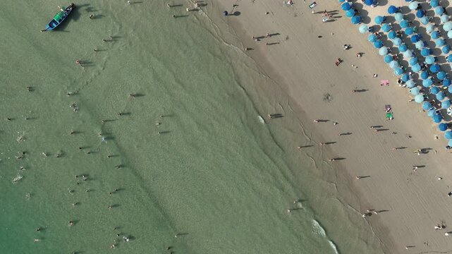 day time phuket island famous crowded beach bay full of blue umbrella coastline aerial topdown panorama 4k thailand