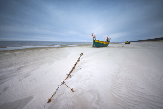View of a traditional wooden fishing boat parked on a wide sandy beach under an overcast sky in Debki, Pomeranian Voivodeship, Poland.