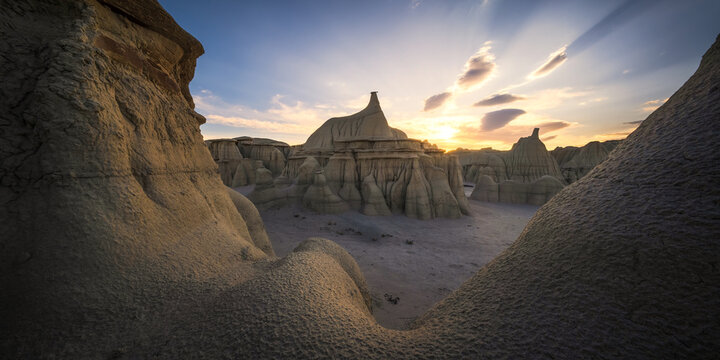 View of the unique hoodoo rock formations at Bisti Badlands under a golden sunset sky in San Juan County, New Mexico, United States.