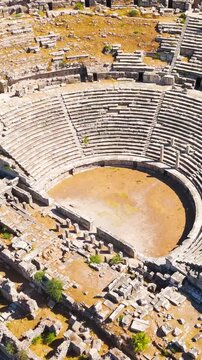 Vertical video. Balat, Turkey. Ancient Theatre of Miletus, sweeping semicircular stone cavea with radial stairways and arched entrances, aerial view over extensive archaeological ruins under bright s