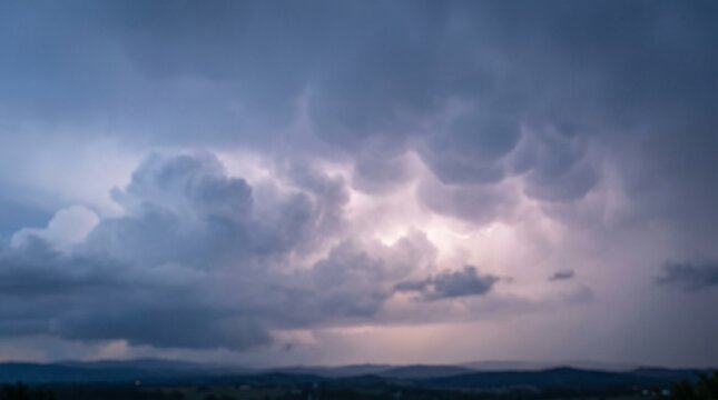 Soft diffuse storm glow breaking through dense overcast dark clouds before a severe thunderstorm over distant hills