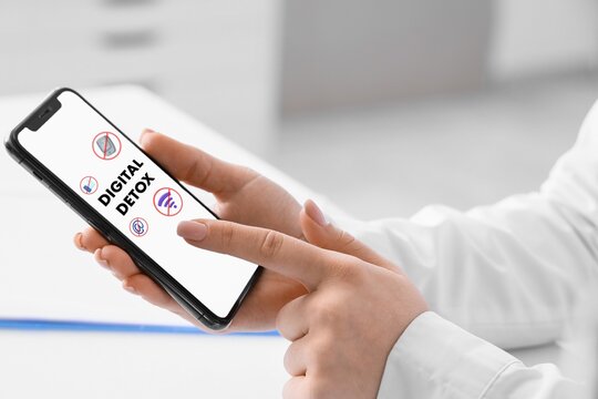 Woman using smartphone with text DIGITAL DETOX on screen, closeup