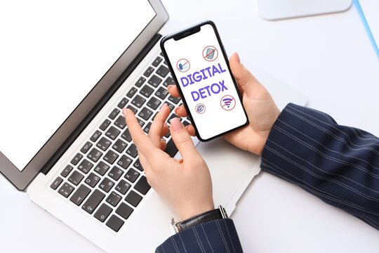 Hands of businesswoman holding smartphone with text DIGITAL DETOX on screen in office, top view