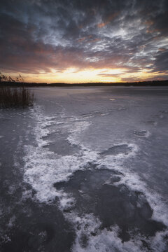 View of a frozen lake with ice patterns and snow under a dramatic sunset sky with orange clouds Gorzyce, Silesian Voivodeship, Poland.