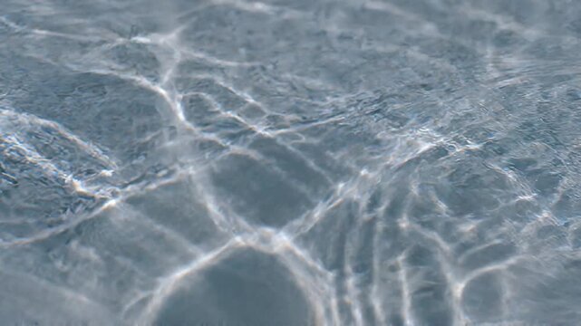Beautiful close-up of clear, shallow water with shimmering sun caustics and gentle ripples. Perfect for a clean, refreshing, and serene aquatic background.