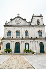 Obraz premium Ancient Portuguese St Lazarus Church stone facade with traditional green wooden doors and bell tower during cloudy summer day in Macau travel destination