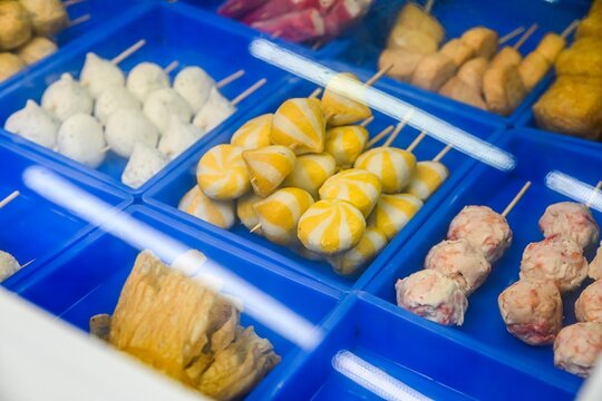 Assorted colorful Chinese fish balls on skewers with striped sea urchin buns inside blue plastic trays at local street food stall in Taipa Macau