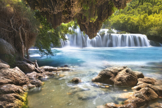 View of Krka National Park featuring the Skradinski Buk waterfall with turquoise water, lush green foliage, and rocky riverbanks Sibenik-Knin County, Croatia.