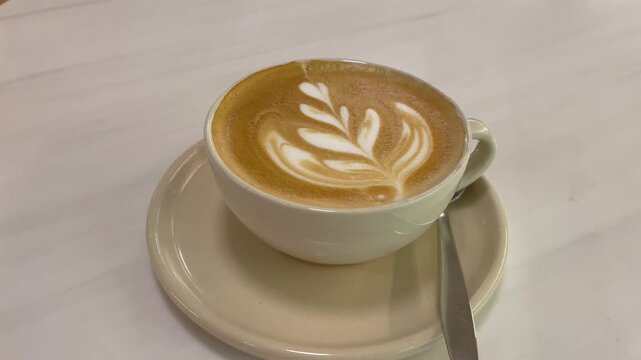 Freshly brewed latte with delicate leaf pattern latte art in white ceramic cup