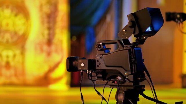 Professional television camera on tripod recording live stage event in broadcast studio.