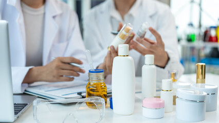 Fototapeta premium Scientists in white coats reviewing cosmetic skincare bottles in a lab, discussing product packaging and formula testing for beauty and personal care development.