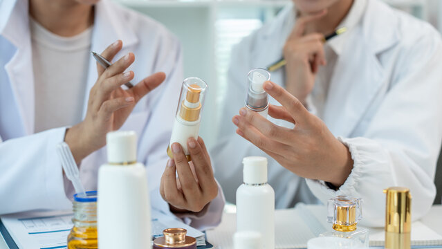 Scientists in white coats reviewing cosmetic skincare bottles in a lab, discussing product packaging and formula testing for beauty and personal care development.