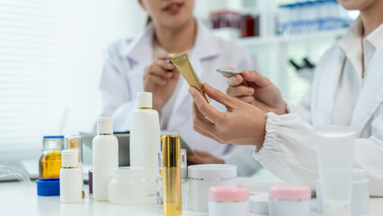 Two female scientists in white lab coats test skincare products at a laboratory table with bottles,...