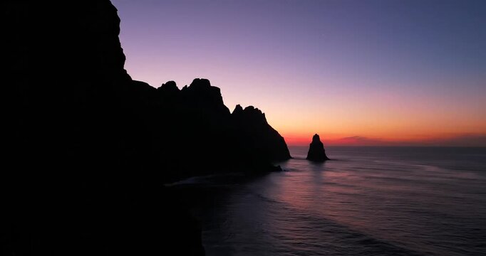 Serene sunset over rocky coastline with gentle waves and distant silhouette of cliffs