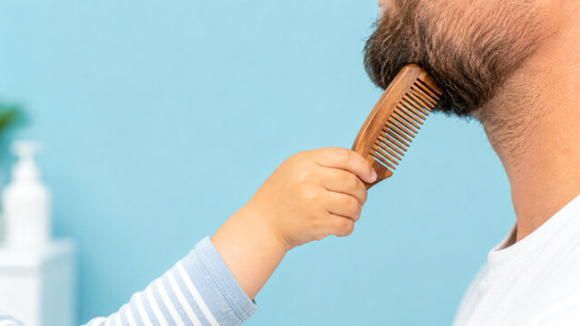 Child hand holding wooden comb near adult male beard
