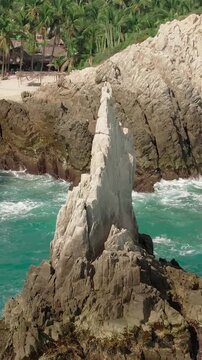 Drone pulls back from Dedo de Dios rock formation as turquoise waves crash along Maruata Beach, Michoacan, Mexico