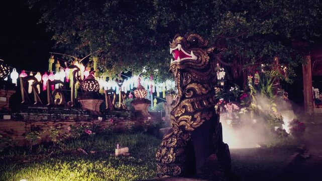 Static medium shot of an ornate golden Lanna-style Singha guardian lion statue with colorful festival lanterns and slowly drifting mist in foreground, mystical and cinematic night atmosphere hazy mist