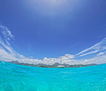 View of a white catamaran sailing on turquoise tropical waters with lush green mountains under a bright blue sky Trou-aux-Biches, Pamplemousses District, Mauritius.