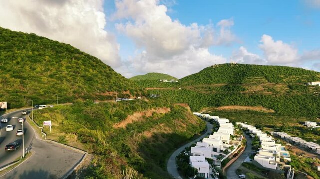 Drone view of contemporary white residential villas located in Indigo Bay on Saint Martin island in the Caribbean Sea. Lush green tropical hills surround the luxury housing development.