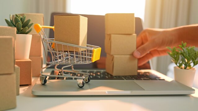 A hand stacking boxes in layers reflects bulk purchasing from e-commerce, emphasizing digital shopping trends, efficient logistics, consumer demand, and online business growth.
