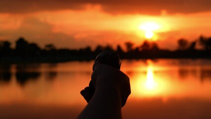 Fototapeta premium A hand points a flashlight at the sunset, representing exploration, curiosity, the pursuit of answers, determination to illuminate uncertainty, and the interplay of technology and natural beauty. 