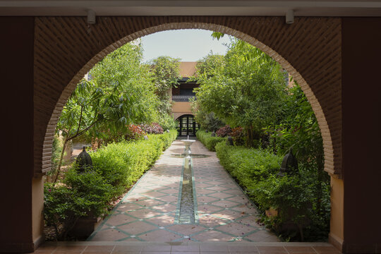 View of a lush courtyard garden with a central water feature and green hedges seen through a brick archway in Agadir, Souss-Massa, Morocco.