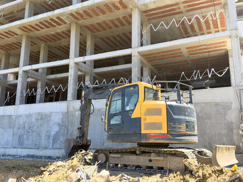 View of a yellow excavator parked at a construction site in front of a multi-story concrete building frame Avcilar, Istanbul, Turkiye.
