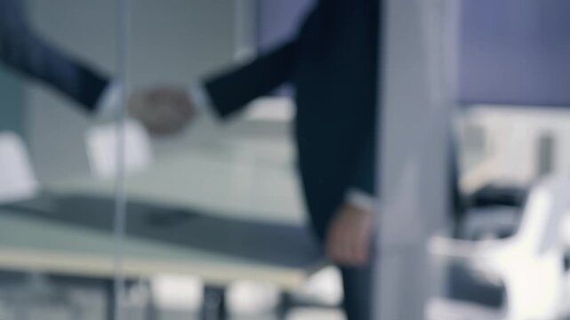 Blurred background of two business people shaking hands, symbolizing a successful partnership, agreement, and collaboration in a modern corporate office setting.