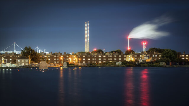 View of Poolbeg Generating Station chimneys and residential buildings at night with reflections on the water in Dublin, County Dublin, Ireland.