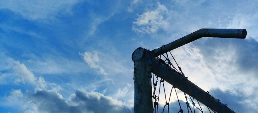 Low angle silhouette of a soccer goal post against a dramatic cloudy blue sky