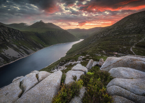 View of Silent Valley Reservoir surrounded by the Mourne Mountains under a dramatic sunset sky with granite boulders in the foreground Newry, Northern Ireland, United Kingdom.