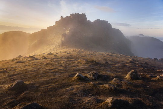 View of Slieve Bearnagh mountain peak with mist rolling over the rocky slopes during a golden sunrise in Newry, Northern Ireland, United Kingdom.