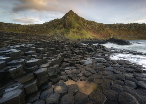 View of the Giant's Causeway featuring interlocking basalt columns along the rugged coastline under a soft sunset sky Causeway Coast and Glens, Northern Ireland, United Kingdom.