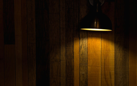 Warm pendant lamp casting soft golden light on a rustic wooden wall in a dark moody interior, ideal for cozy home decor, atmospheric restaurant design, wood texture, lighting and copy space concepts.