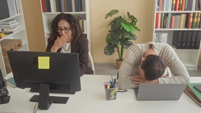 Woman places hand on man's shoulder as he buries his head on a laptop at a desk in an office building; support stress.