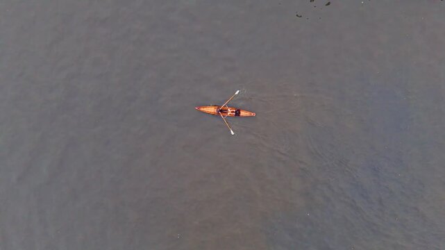 Rower paddling single scull on calm river, aerial view shows solo recreation