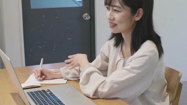 Young asian woman taking notes in notebook while working on laptop