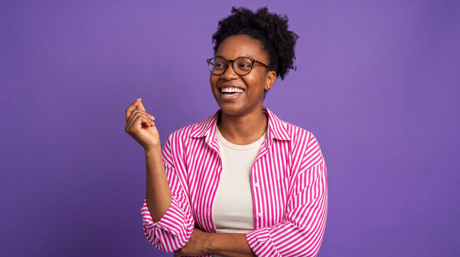 A young woman with glasses and a pink striped shirt smiles brightly while looking to the side. Her left hand is raised with her fingers in a gesture of confidence and excitement.