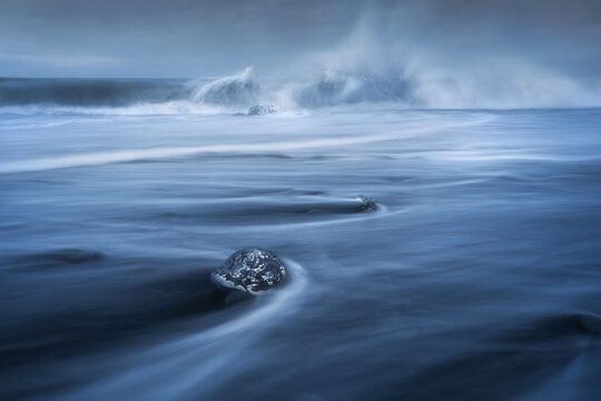 View of ice chunks on Diamond Beach with crashing waves and motion blur on the black sand Sveitarfelagid Hornafjordur, Iceland.