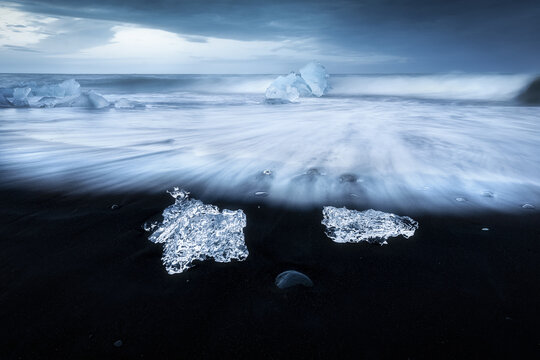 View of Diamond Beach with ice chunks on black volcanic sand and long exposure waves under a dramatic blue sky Sveitarfelagid Hornafjordur, Iceland.