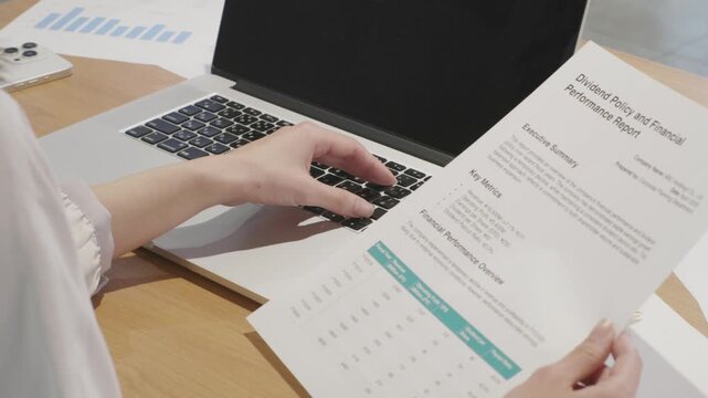 Close-up of woman's hands holding business document while working on laptop
