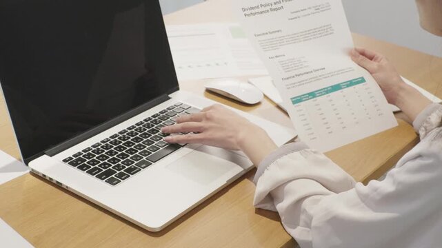 Close-up of woman's hands holding business document while working on laptop