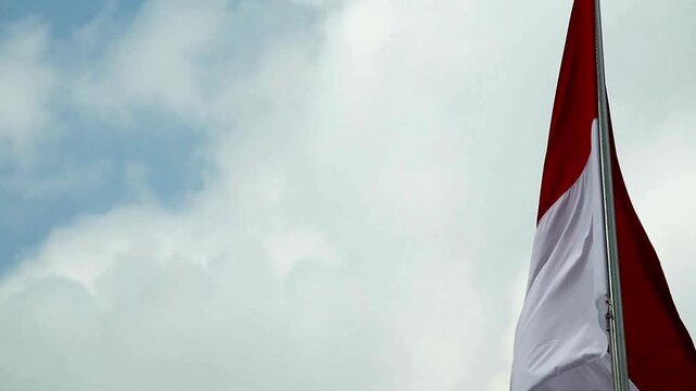 Red and white Indonesian national flag waving in the wind against cloudy sky