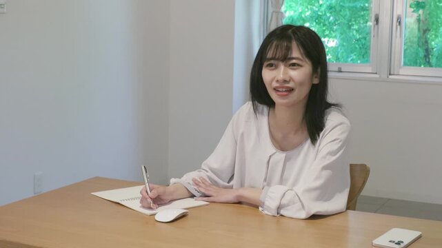 Young asian woman taking notes in notebook while working on laptop