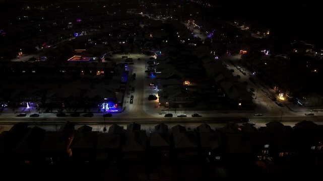 Aerial night footage of a snow-covered residential neighborhood in Edmonton, Alberta, Canada. Slightly lit streets, homes, and urban infrastructure, winter cityscape against the snowy winter