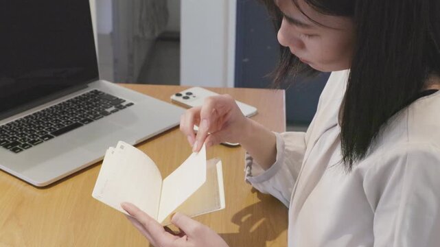Asian woman looking at bank passbook at desk