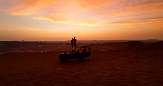 Couple standing on dune buggy in Huacachina desert enjoys vivid golden sunset