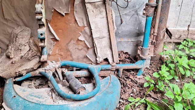 Abandoned motorcycle part lying in a neglected rustic junkyard surrounded by rusted metal, weathered debris, industrial decay, and an authentic abandoned outdoor atmosphere