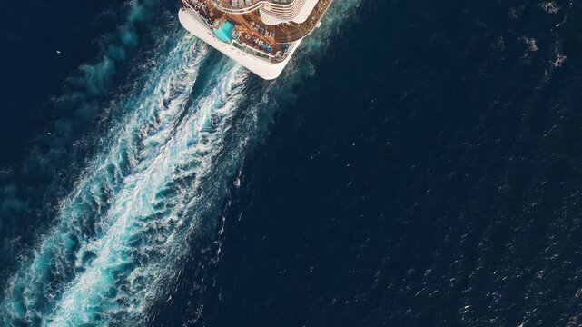 Magnificent aerial view of a large luxury cruise liner sailing on the deep blue sea, leaving a beautiful white wake behind as the sun shines on the upper decks and swimming pools
